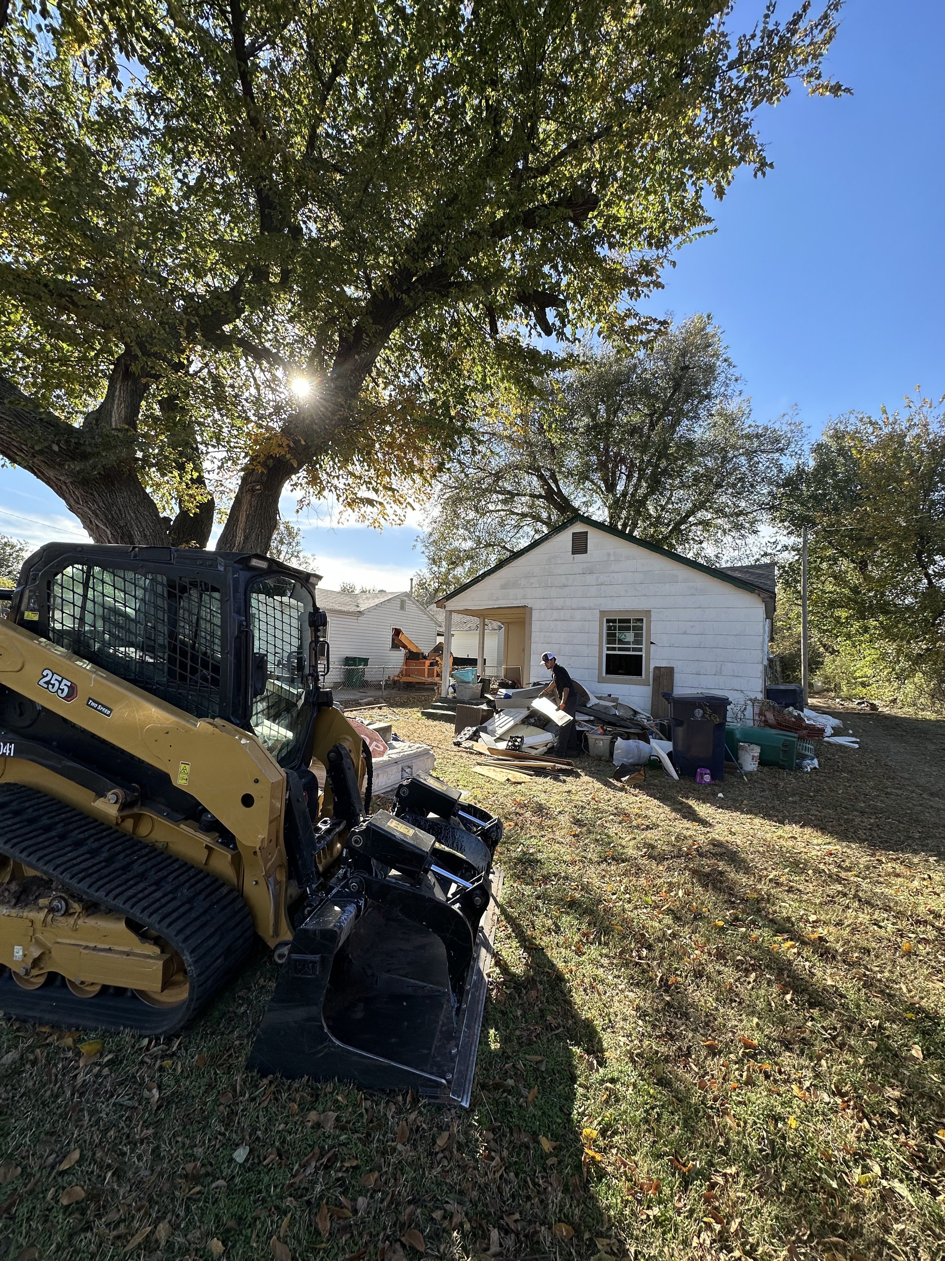 Big Trucking LLC Caterpillar 255 track loader at junk removal site in Oklahoma City with debris pile near white house