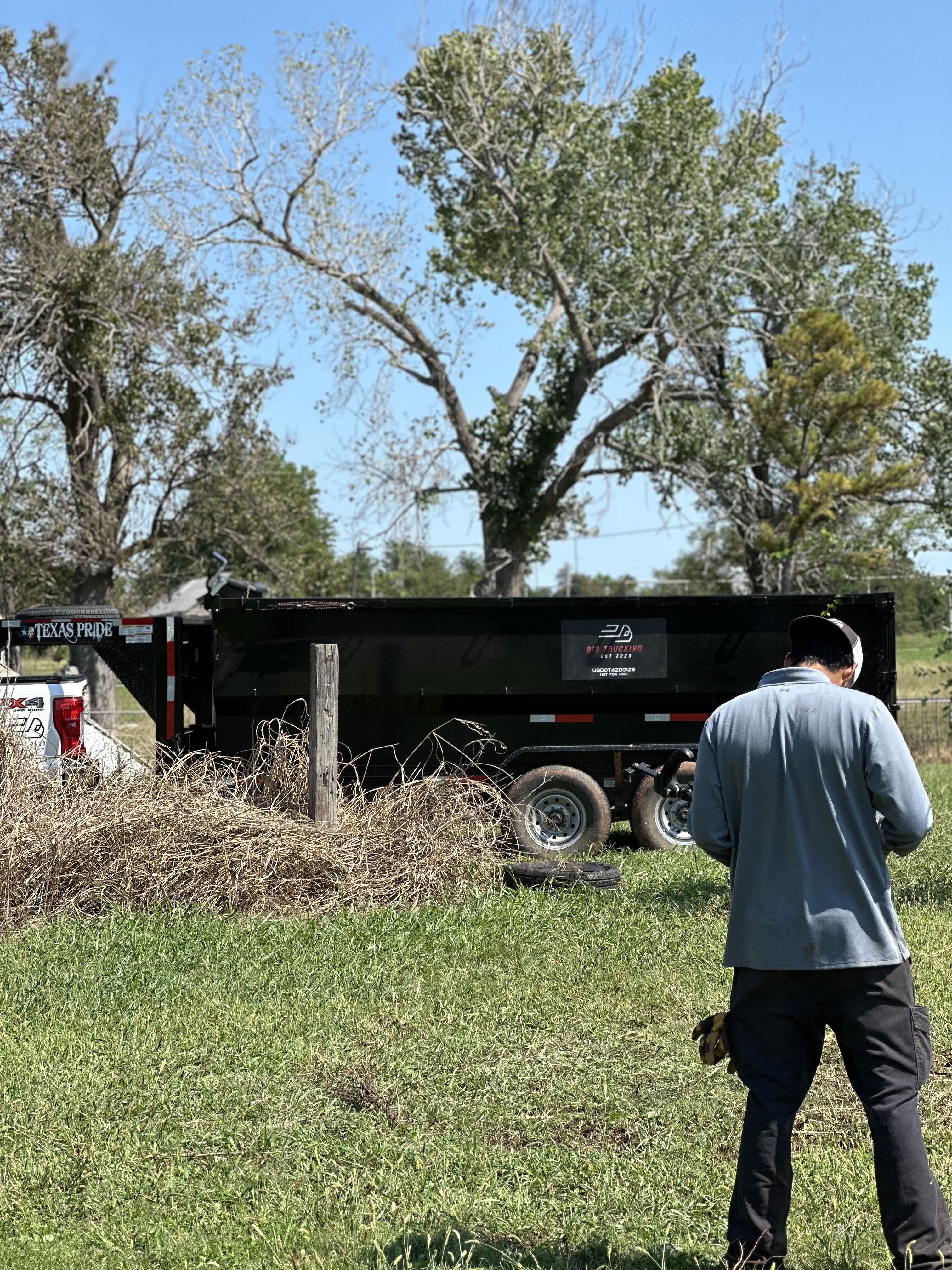 Big Trucking LLC team member near black dump trailer in Oklahoma field for hauling services
